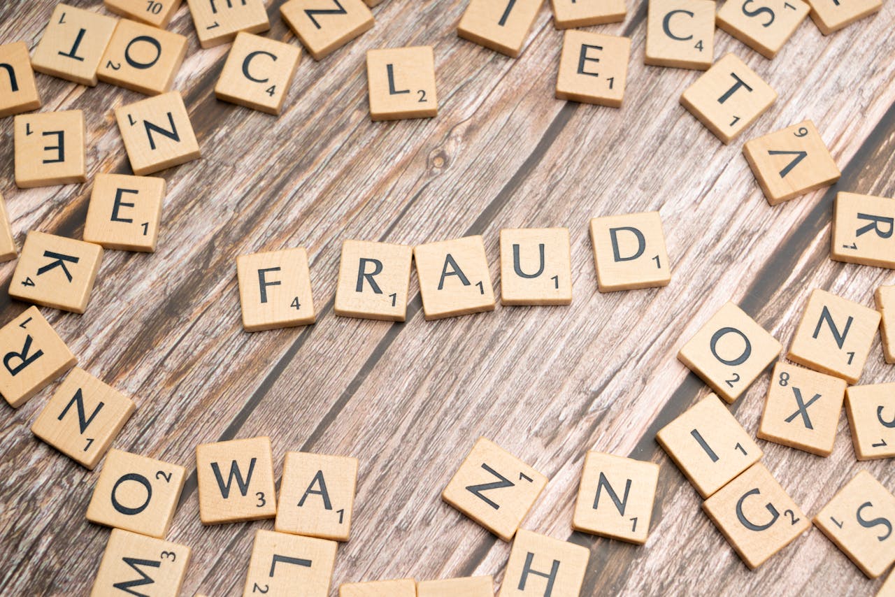 services-01 Alphabet tiles arranged to spell 'fraud' on a wooden surface, symbolizing deception.
