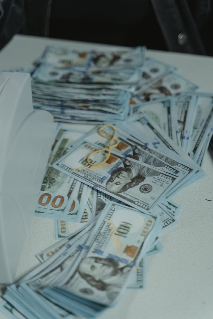A pile of US dollar bills neatly stacked and secured with a rubber band on a white surface.
